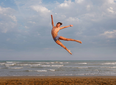 沙滩上的运动少年在海阔天空的背景下跳跃