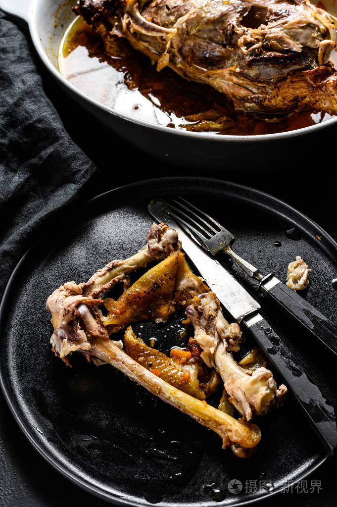 烤盘里的一盘鸡骨头和一个鸡骨架晚餐剩菜黑色背景俯视图