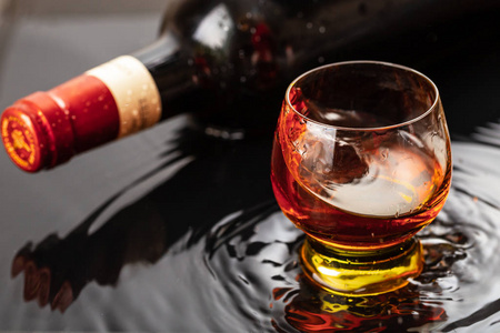 一瓶红酒加酒杯.水溅落在黑色的倒影上.照片