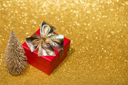 Red gift box with gold bow and little christmas tree on gold gli