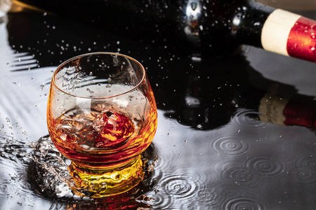 一瓶红酒加酒杯.水溅落在黑色的倒影上.照片