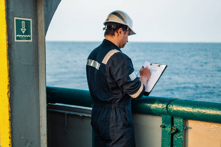 在海上船舶或船舶的甲板上，穿戴个人防护装备的甲板驾驶员。他填写检查表。海上文书工作