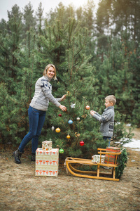 冬天和人的概念母亲带着孩子在森林里装饰一棵户外圣诞树