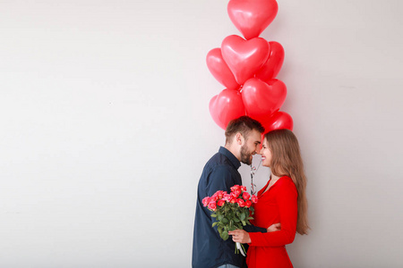 幸福的年轻夫妇，心形气球和鲜花在浅背景上。情人节庆祝