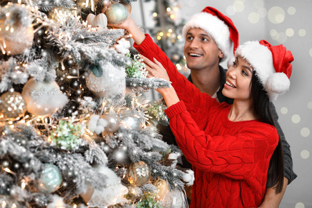 幸福的年轻夫妇戴着圣诞帽装饰圣诞树