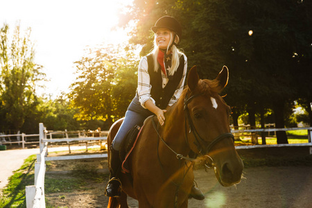 照片中的金发女子戴着帽子骑马在院子里