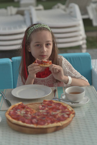 咖啡馆里拿着披萨的年轻女人的画像。9岁女孩假期在一家夏日咖啡馆吃披萨