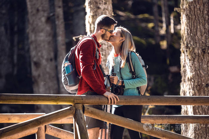两个背着背包的旅行者站在森林里的木桥上亲吻