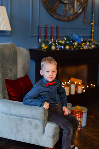 漂亮的男孩坐在一张装饰新年的扶手椅上。
