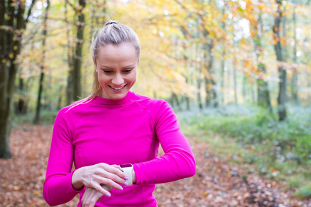 Woman Exercising In Autumn Woodland Looking At Activity Tracker 