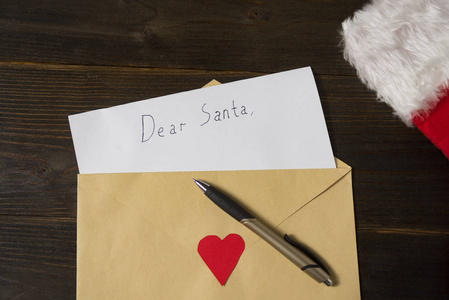 给圣诞老人的信装在信封里。木制背景上的钢笔和帽子。圣诞节概念