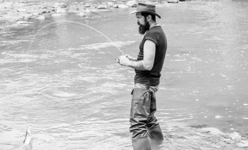 钓鱼的乐趣在于捕鱼。钓鱼男性嗜好。凶残的男人穿着胶靴站在河水里。费希尔周末活动。捕鱼设备的渔夫。鱼钩上的鱼。野外休闲