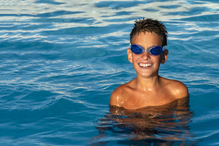 游泳池里戴着水杯的快乐微笑的男孩。