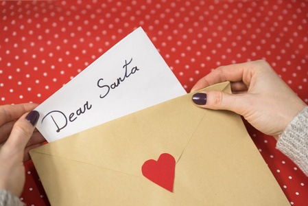 女的手把一封写给圣诞老人的信放在信封里。木质背景。特写