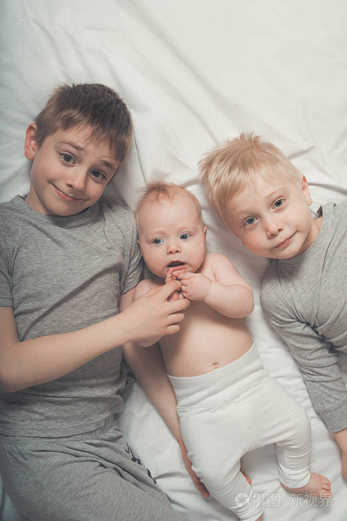 两个哥哥和最小的婴儿躺在一张白色的床上。快乐的童年，大家庭