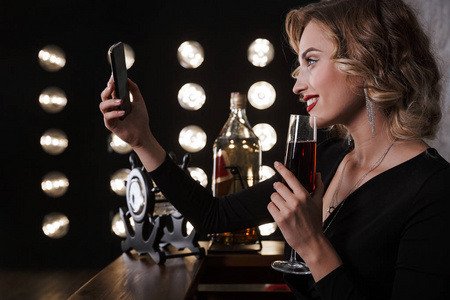 图为年轻金发女子在酒吧里用手机喝红酒