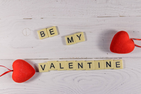 Red hearts and Be my Valentine text on white wooden background