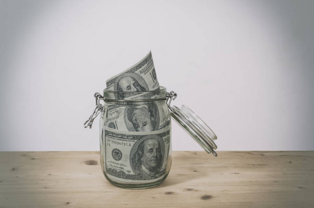 Dollar bills in glass jar on wooden table. 