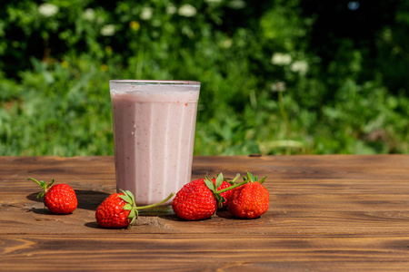 Glass of fresh strawberry smoothie on a wooden table outdoor 