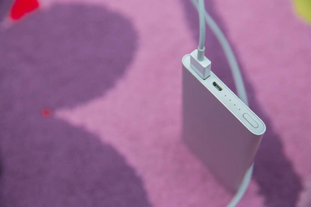 能源银行。智能手机充电银电源通过螺旋USB电缆。智能手机在粉红色地毯上充电。
