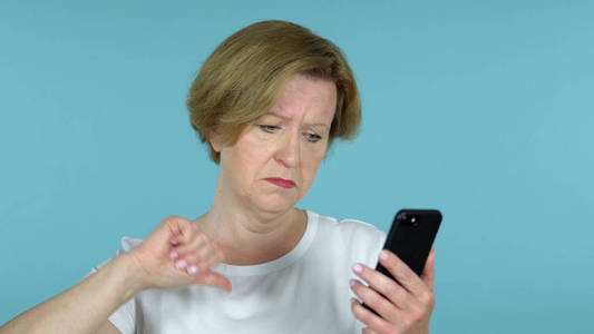 老妇人对失去的反应和使用隔离在蓝色背景上的智能手机