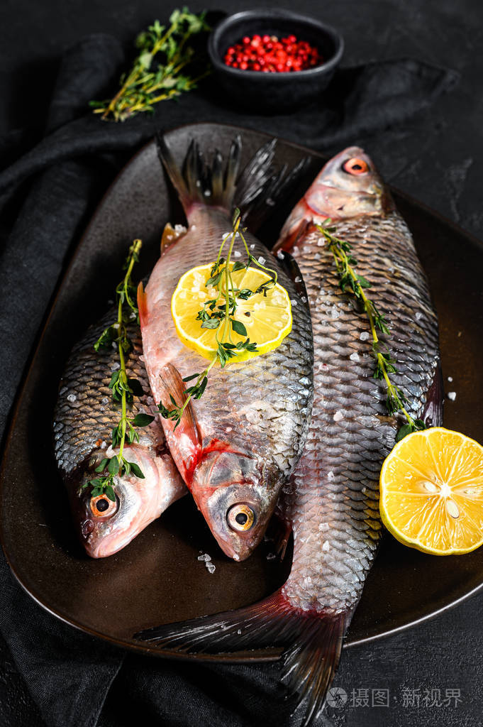 生鲫鱼配柠檬和百里香放在黑色盘子里有机鱼河黑色背景俯视图