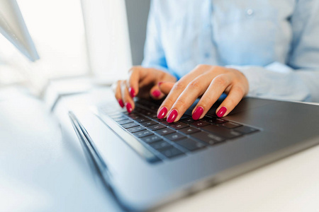 在笔记本电脑键盘上用明亮的指甲打字的女性手