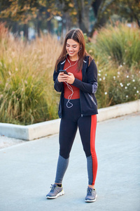 Modern young woman with cellphone making pause during jogging  