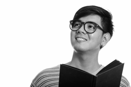 摄影棚拍摄年轻快乐的亚洲男人一边拿着书一边思考一边微笑