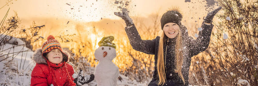 一家人穿着温暖的衣服。微笑的母子俩在户外堆雪人。冬季活动概念横幅，格式长