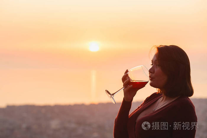 夕阳山上的女人拿着红酒近距离的手持酒杯优雅的女人在夕阳下欣赏美丽