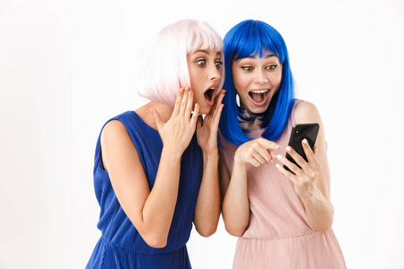 两个震惊的女人戴着蓝色和粉色的假发，指着手指看着手机