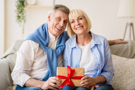 幸福的老夫妻手拿礼品盒，对着镜头微笑