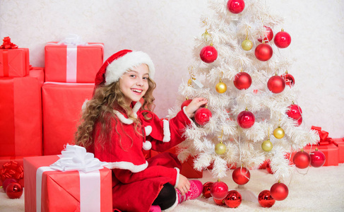 珍惜节日活动。孩子喜欢家庭传统。平安夜概念。加入圣诞庆祝活动。女孩微笑着可爱的圣诞老人坐在圣诞树旁。装饰圣诞树的孩子