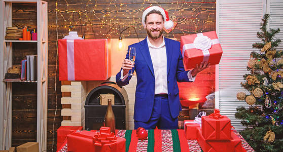 满脸胡须的商人拿着一杯香槟和礼盒庆祝新年。新年快乐，圣诞快乐。欢快的经理正装庆祝公司聚会。新年晚会。干杯
