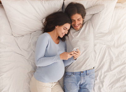 孕妇和丈夫在床上休息时使用智能手机