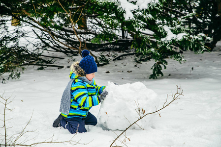 可爱的小男孩在堆雪人。滚大雪球