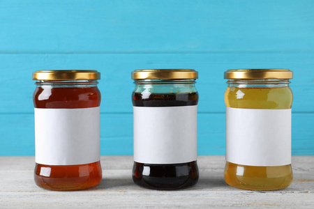 Jars of organic honey with blank labels on wooden table against 