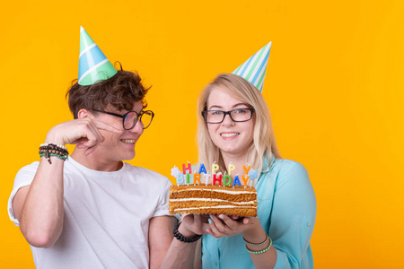 戴着纸帽,拿着蛋糕,站在黄色的背景下,做了一张傻乎乎的脸,祝生日快乐