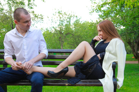 坐在长椅上的浪漫情侣拥抱在一起，享受爱情。一个男人给女孩做足部按摩