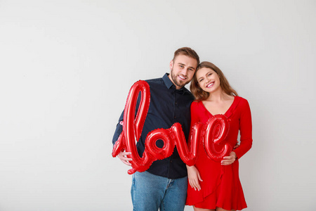 一对幸福的年轻夫妇，在浅色背景上画着爱字的气球。情人节庆祝