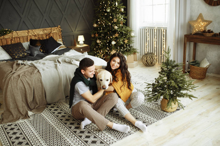 这对幸福的夫妇和一只狗坐在床边，圣诞节。在家过年。家庭和日期