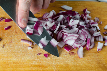砧板食物一个男人用菜刀在一个木制的砧板上切红洋葱.手放紧.
