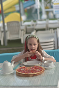 咖啡馆里拿着披萨的年轻女人的画像。9岁女孩假期在一家夏日咖啡馆吃披萨
