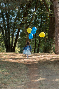 小可爱的女孩拿着一堆气球在公园里跑。跑开了。快乐童年的概念。