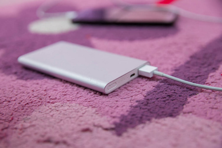 智能手机充电银电源通过螺旋USB电缆。智能手机在粉红色地毯上充电。能源银行。