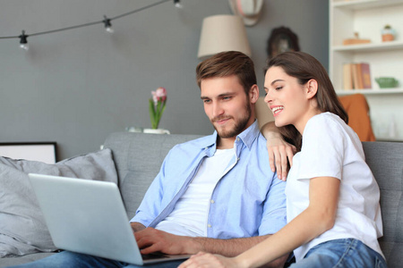 年轻夫妇在家里上网购物，沙发上放着笔记本电脑。
