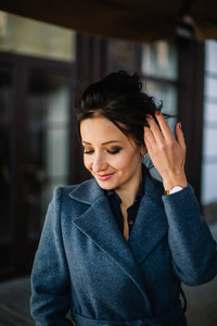 Elegant brunette woman with curly hair in a blue coat corrects a