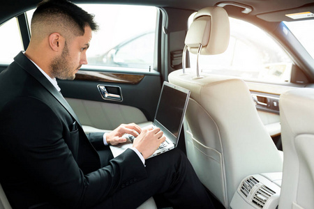 有魅力的男人坐在豪华轿车或汽车里，用笔记本电脑工作