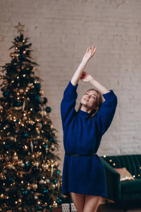 一个年轻漂亮的女人穿着蓝色毛衣在圣诞树的背景上。